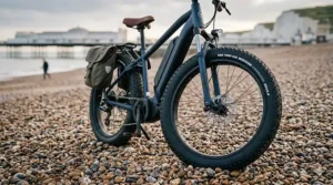 Alt text for image 6: A detailed close-up of high-volume fat tyres on an electric bike parked on a Brighton pebble beach, showcasing the stability and cushioning required for varied British terrain.