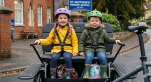 Interior view of a cargo bike box featuring padded seats and 3-point safety harnesses for two primary school children.