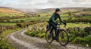 A close-up style portrait of the female cyclist riding her electric gravel bike on a gravel track, showcasing her green cycling jacket, helmet, and the bike's front cockpit frame.