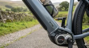 Close-up photograph of a grey electric touring bicycle frame downtube, showcasing the integrated high-capacity battery pack with a glowing LED charge-level indicator, fitted with a water bottle cage.
