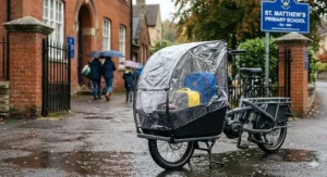 An electric cargo bike with a transparent waterproof rain cover parked outside a UK primary school.