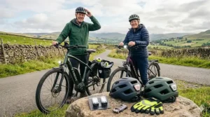 Two cyclists preparing for a ride with safety helmets, lights, and high-visibility gloves displayed on a rock.