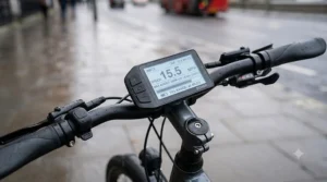A detailed close-up illustration of the e-bike's handlebar display unit, showing legal UK assist speed (15.5 mph), power mode, and battery status, set against a wet London background with a red bus.