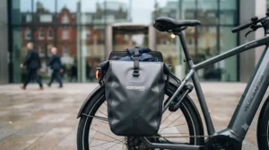 Rear pannier rack loaded with a laptop bag on a GPS-enabled commuter e-bike outside an office building.