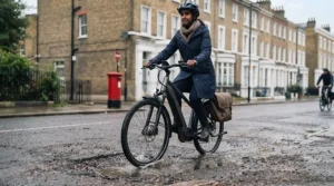 A commuter riding a suspension e-bike smoothly over rough city tarmac and potholes on a typical British road.